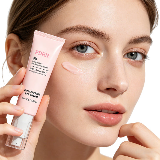 Kvinna håller PDRN Eye Cream ögonkräm intill ansiktet med en klick kräm på kinden